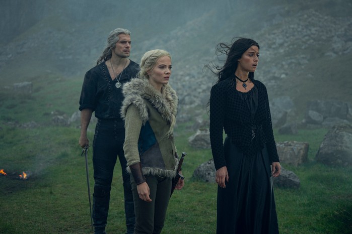 Henry Cavill, Freya Allan and Anya Chalotra in The Witcher season 3, standing at the bottom of a mountain