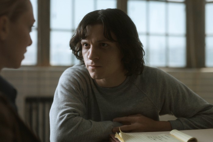 Tom Holland in The Crowded Room with long hair, leaning on a table